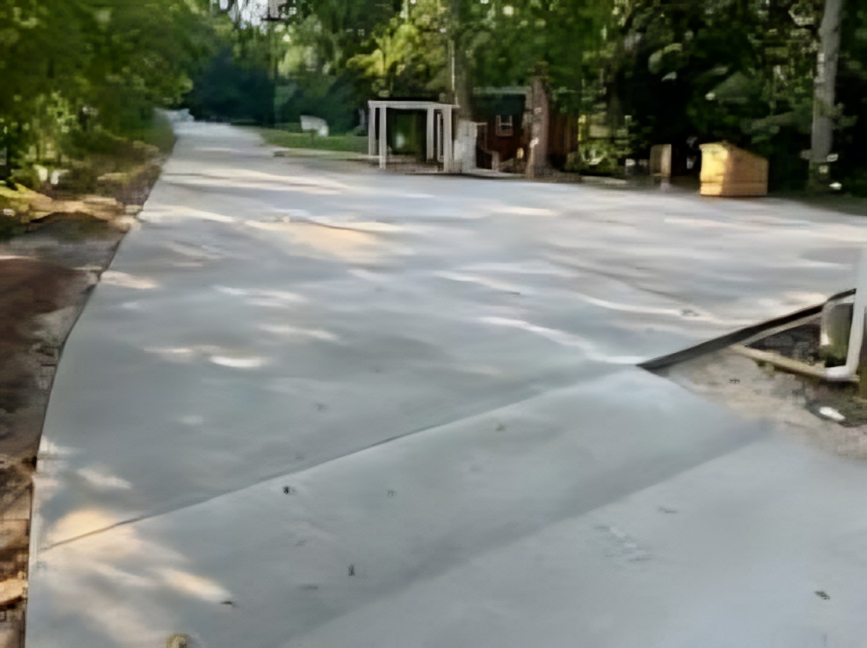 A concrete driveway leading to a house surrounded by trees.