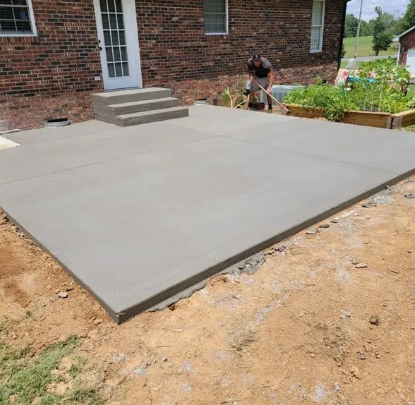 A man is working on a concrete patio in front of a brick house.