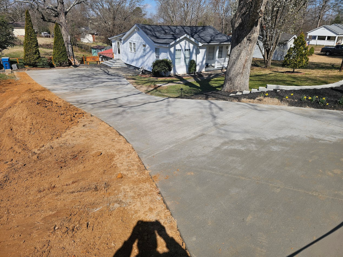 A shadow of a person is cast on a concrete driveway in front of a house.