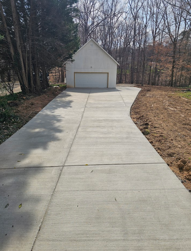 A concrete driveway leading to a garage in the woods.