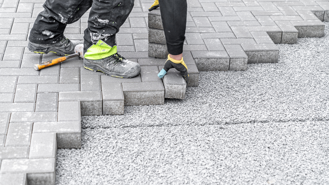 A man is laying bricks on a sidewalk.