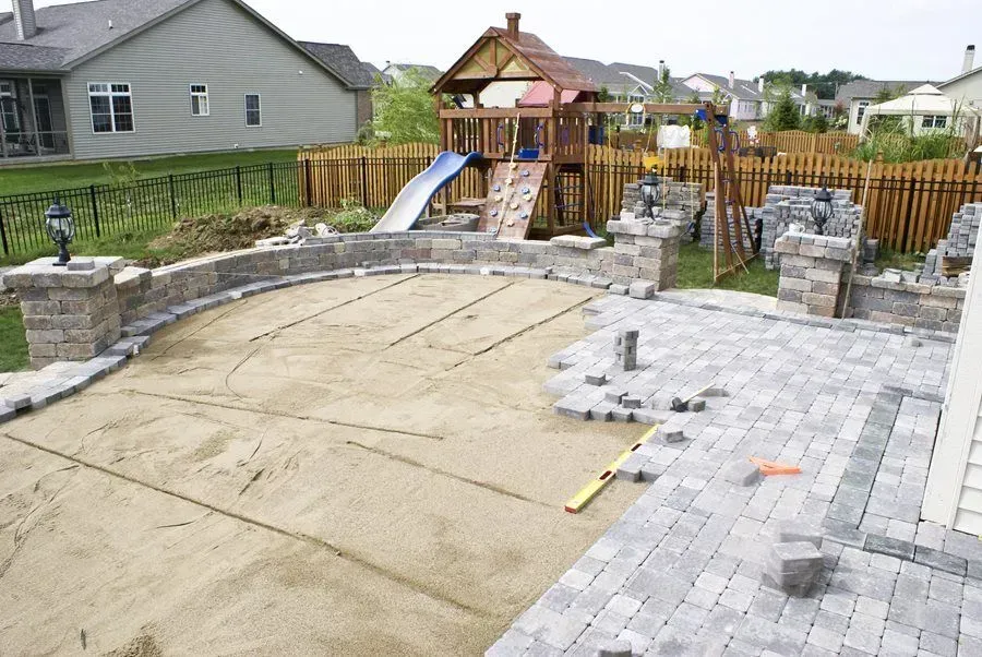 A patio is being built in a backyard with a playground in the background.