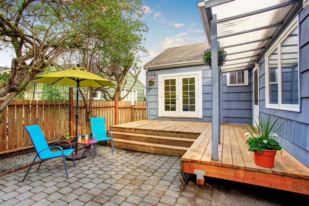 Patio With Blue House, Wooden Deck, Chairs, Yellow Umbrella, and Stone Path — CJ Custom Carpentry in Lake Cathie, NSW