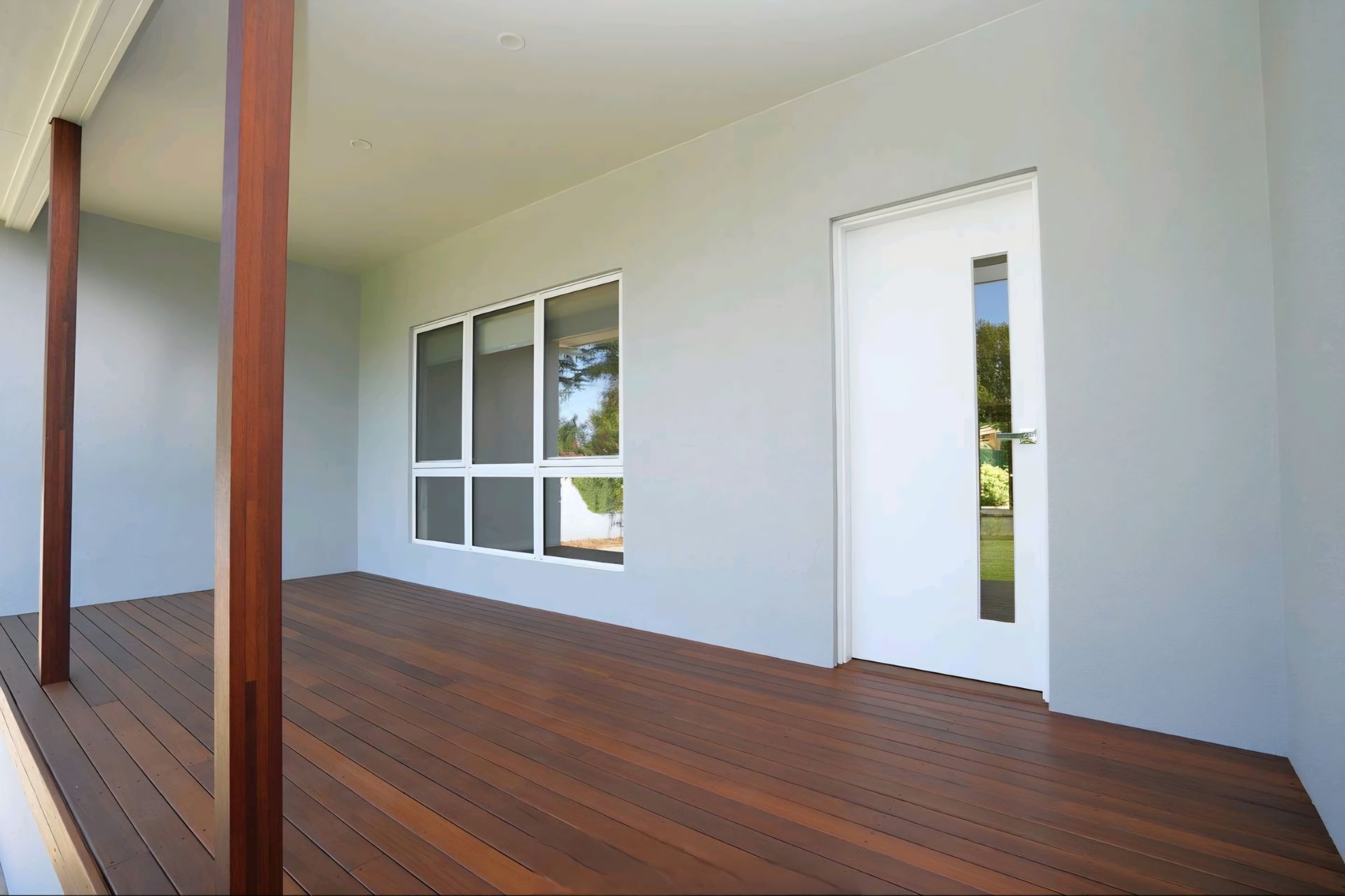 Covered porch with wood flooring, grey walls, and windows, and a white door with a window panel — CJ Custom Carpentry in Port Macquarie, NSW