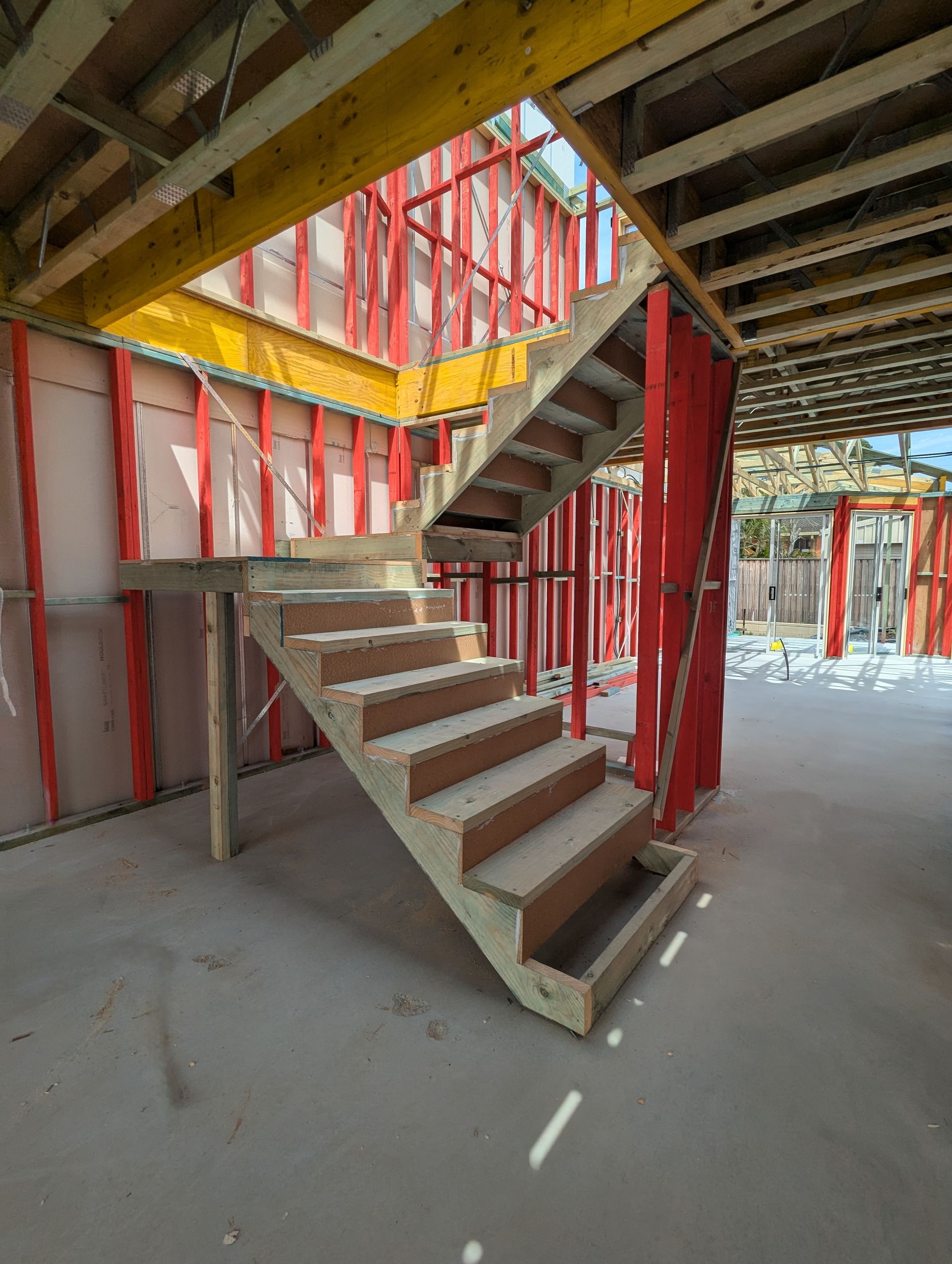 Wooden staircase under construction, framed by red walls and yellow beams in an unfinished building — CJ Custom Carpentry in Port Macquarie, NSW