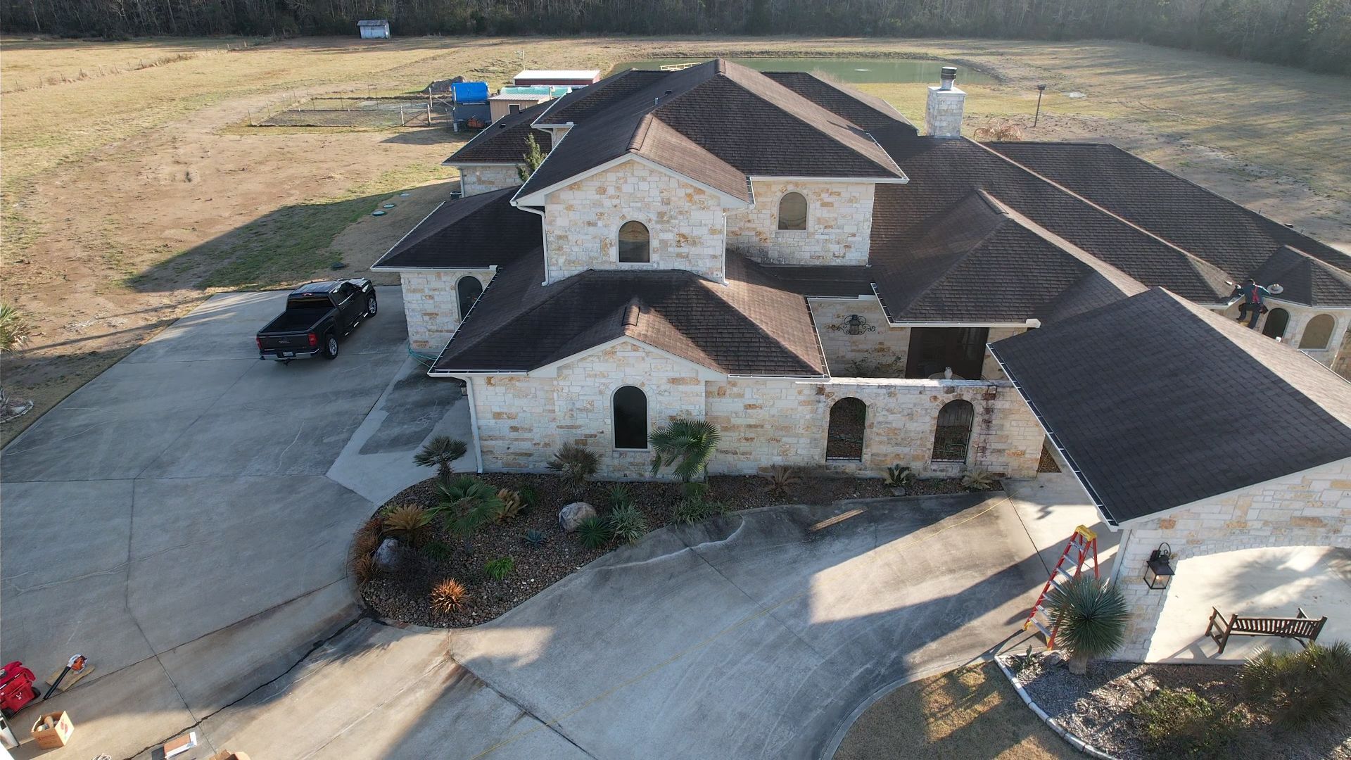 Large stone house with dark roof, long driveway, and a black truck parked out front.