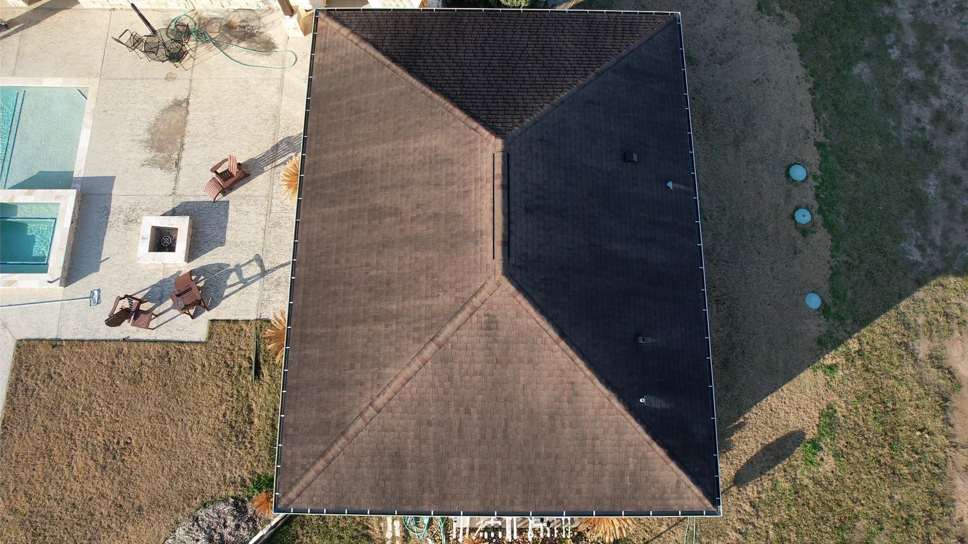 Overhead view of a brown roof with a central vent, next to a pool and lawn.