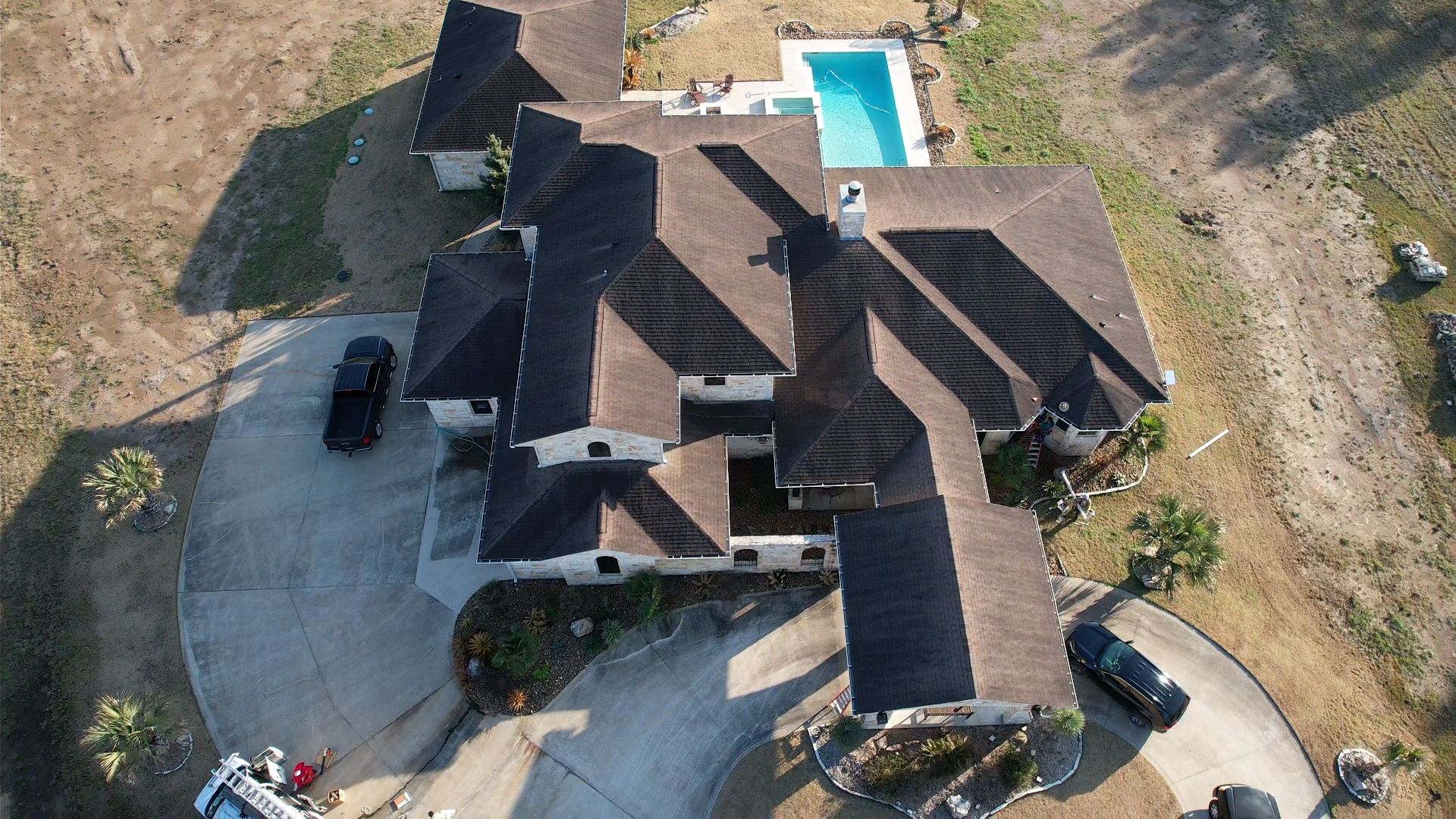 Aerial view of a large house with a dark roof, driveway, and pool.