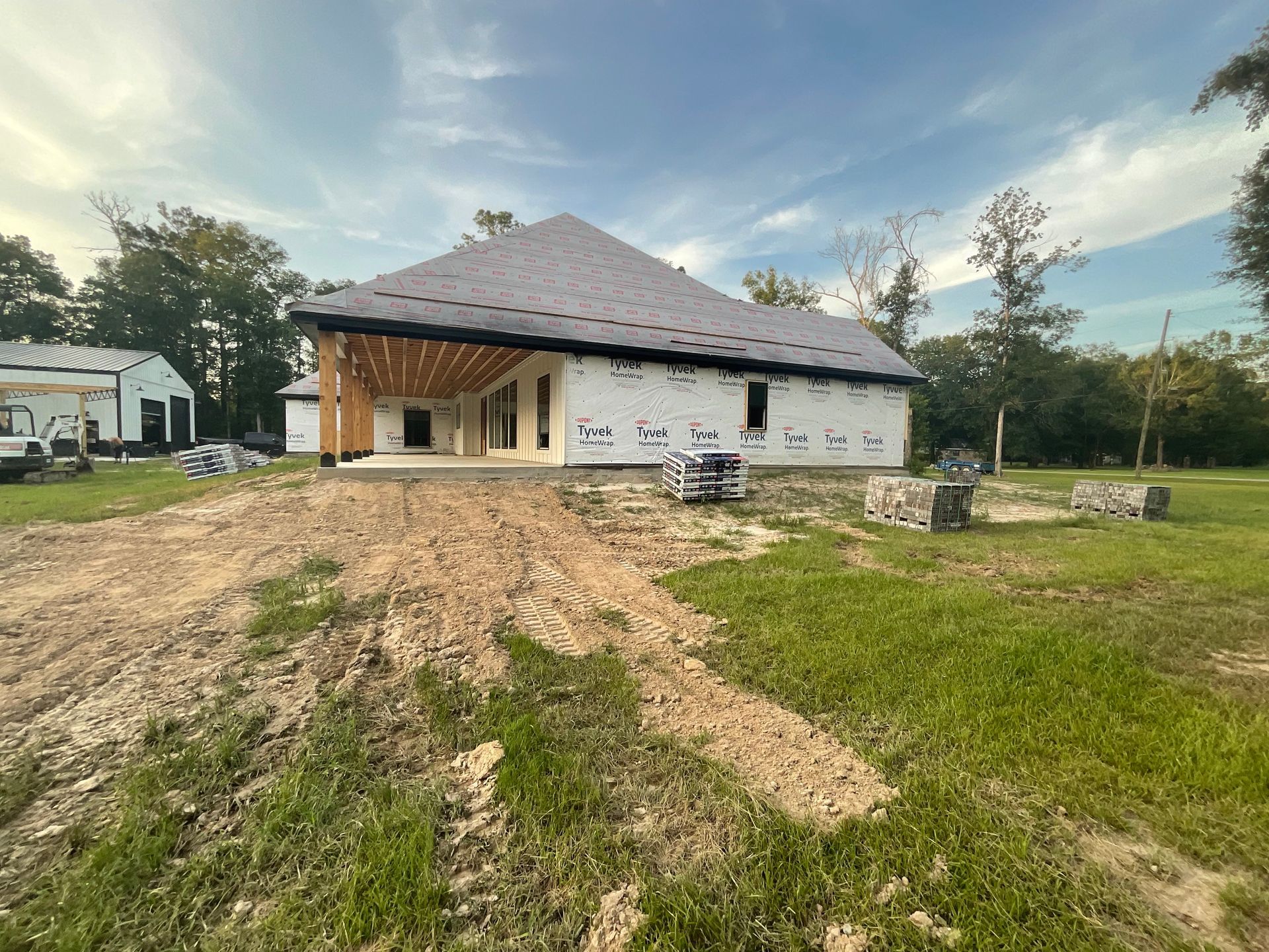 New house under construction with tarpaper roof and wooden beams in a field.
