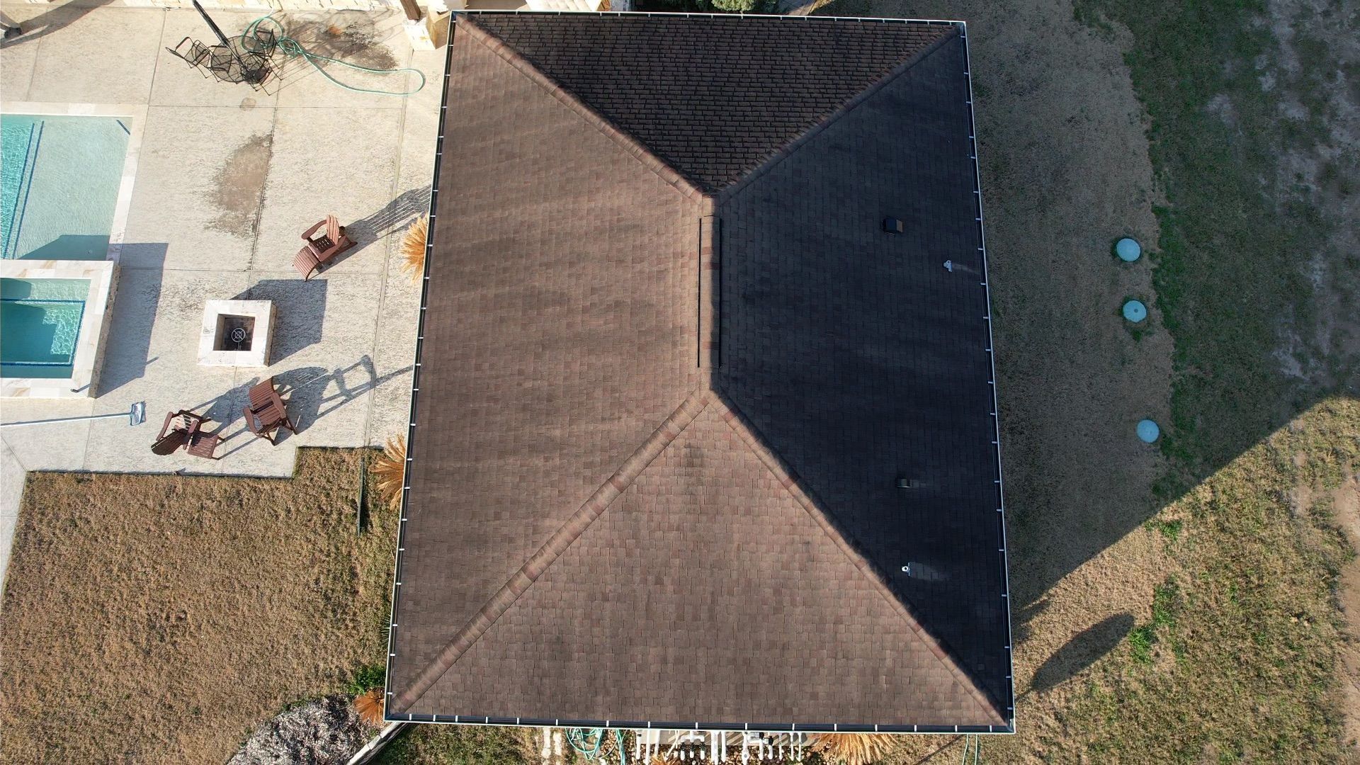 Overhead view of a house with a brown roof, pool, and yard.