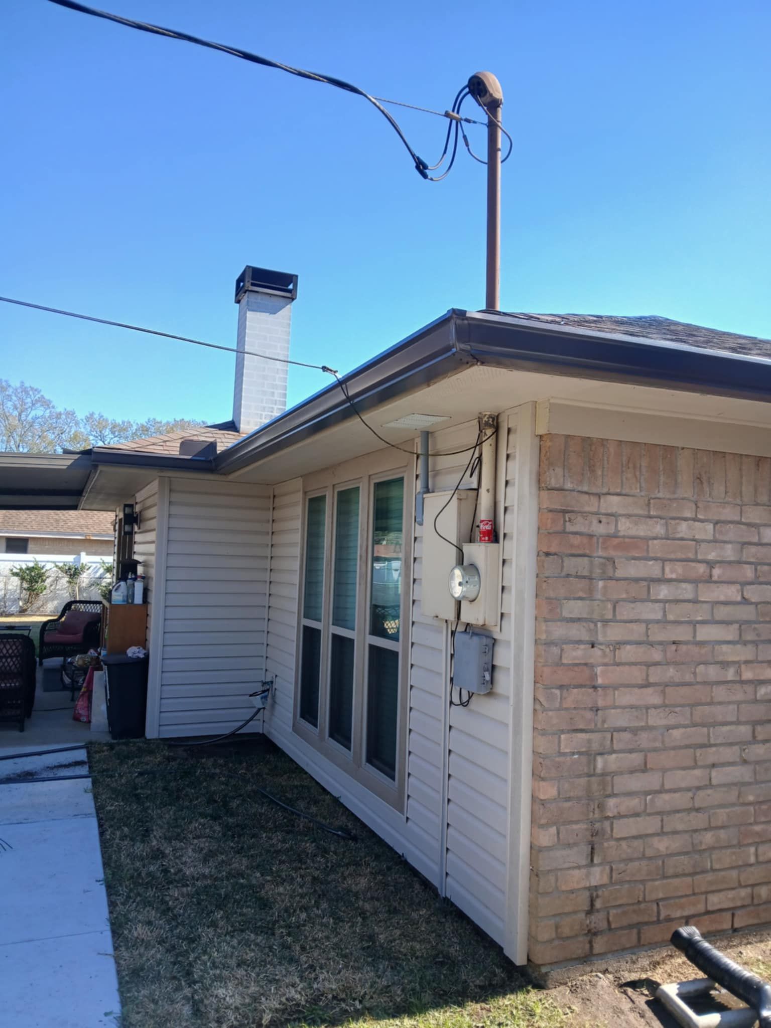 Side view of a house with white siding, brick wall, chimney, and power meter on a sunny day.
