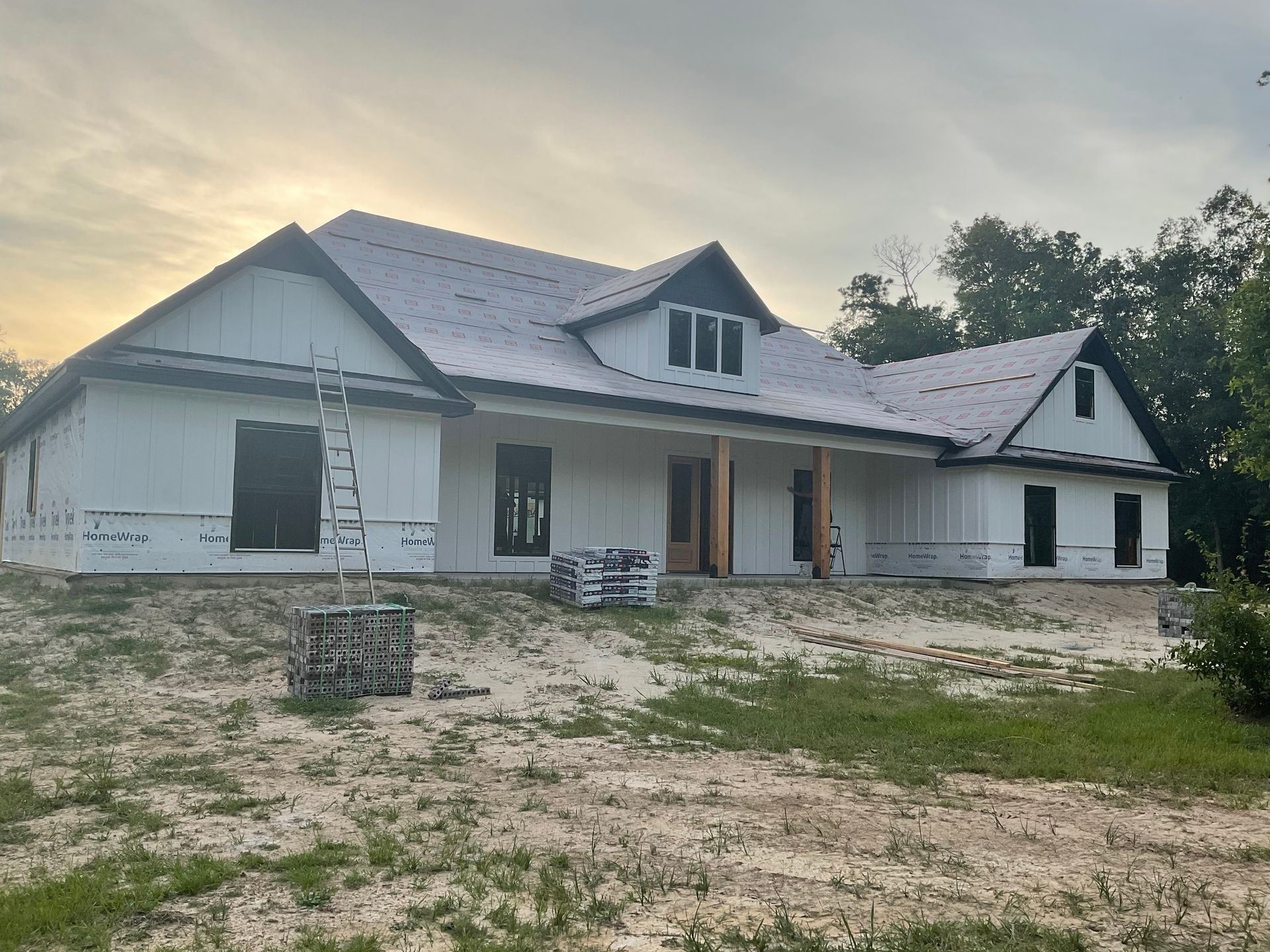 House under construction with white siding, dark trim, and a partially covered roof.