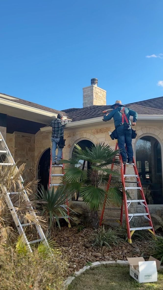 Two workers on ladders install gutters on a house under a blue sky.