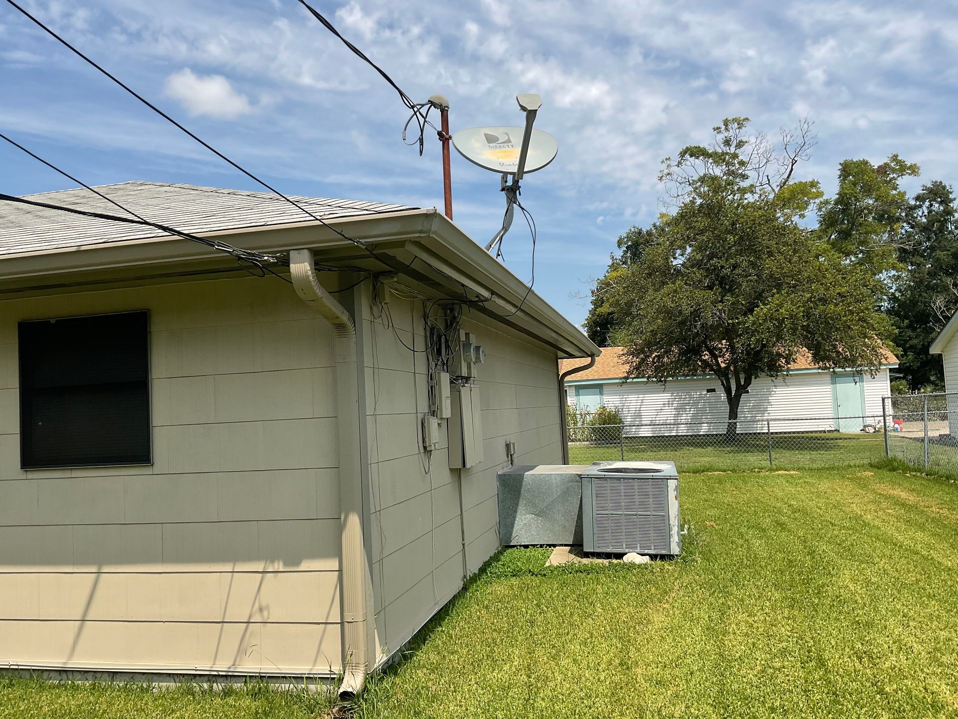 Back of a house with a window, air conditioning unit, and satellite dish. Green grass and sky.