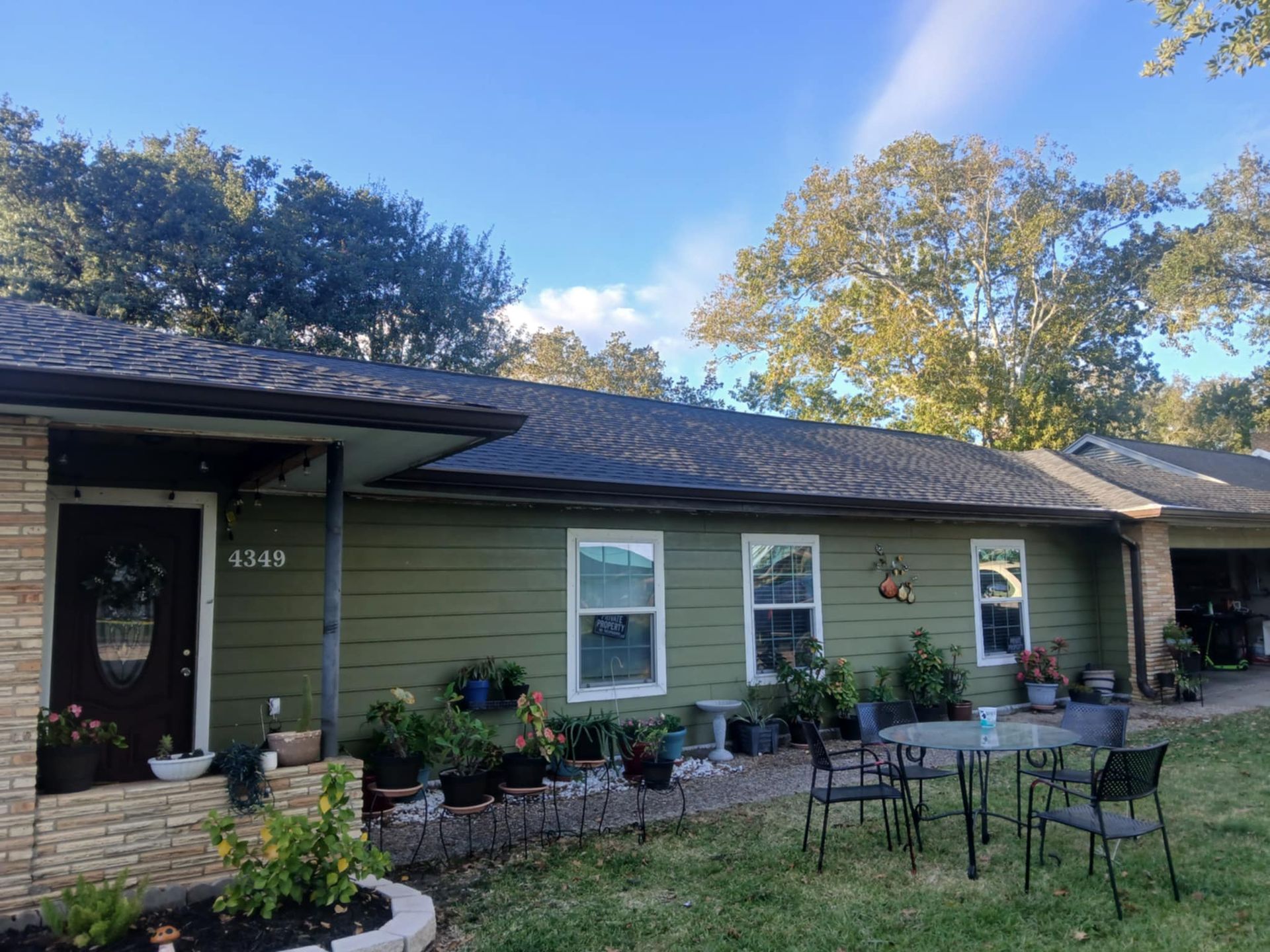 Green house with a brown roof and a small table and chairs in the yard.