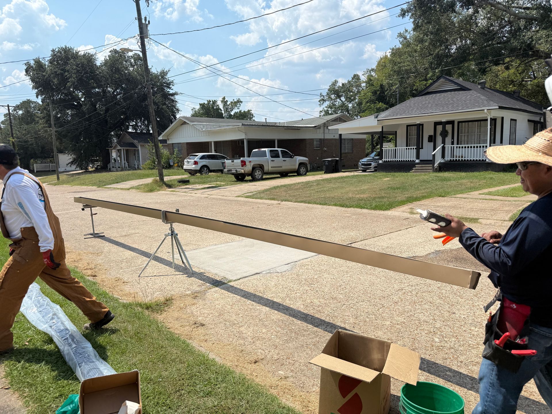 Two men installing gutter along a residential street. One sprays, the other steadies the gutter.