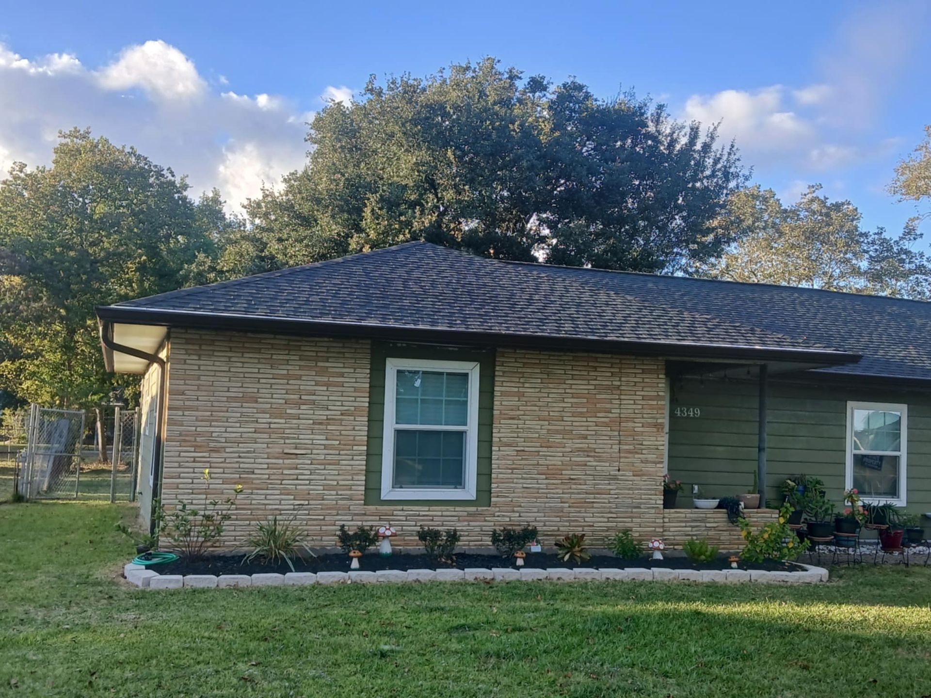 Tan brick-like siding home with green trim and a dark roof under a cloudy sky.