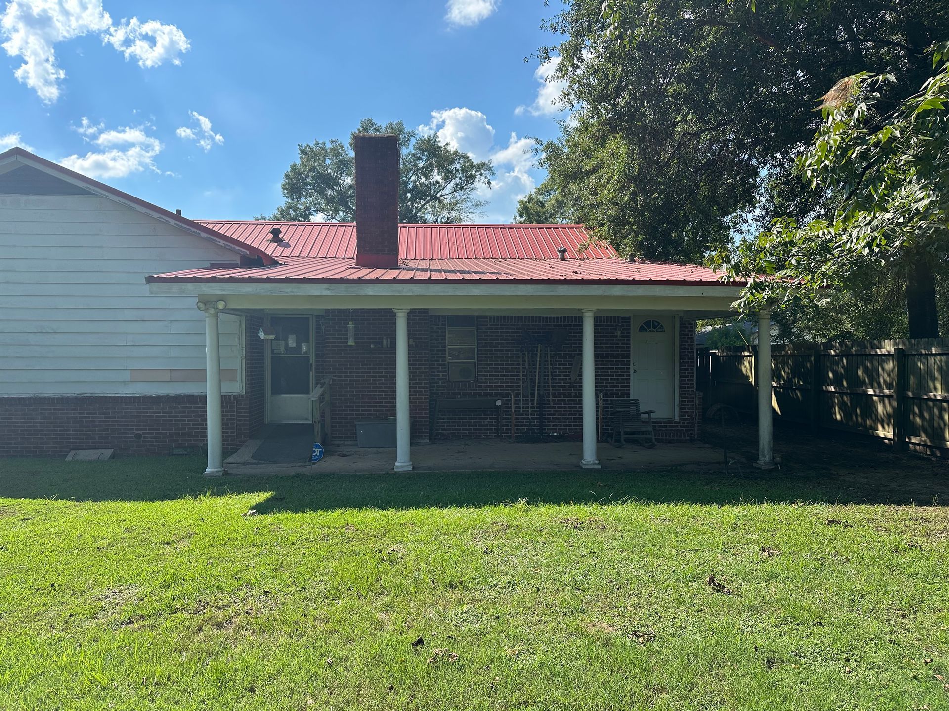 Small house with red roof, front porch, brick chimney, and green yard.