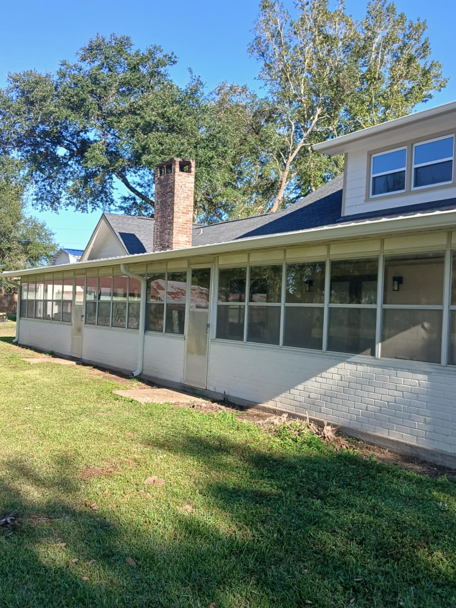 Backyard with screened porch, brick chimney, and lush green lawn under a clear sky.