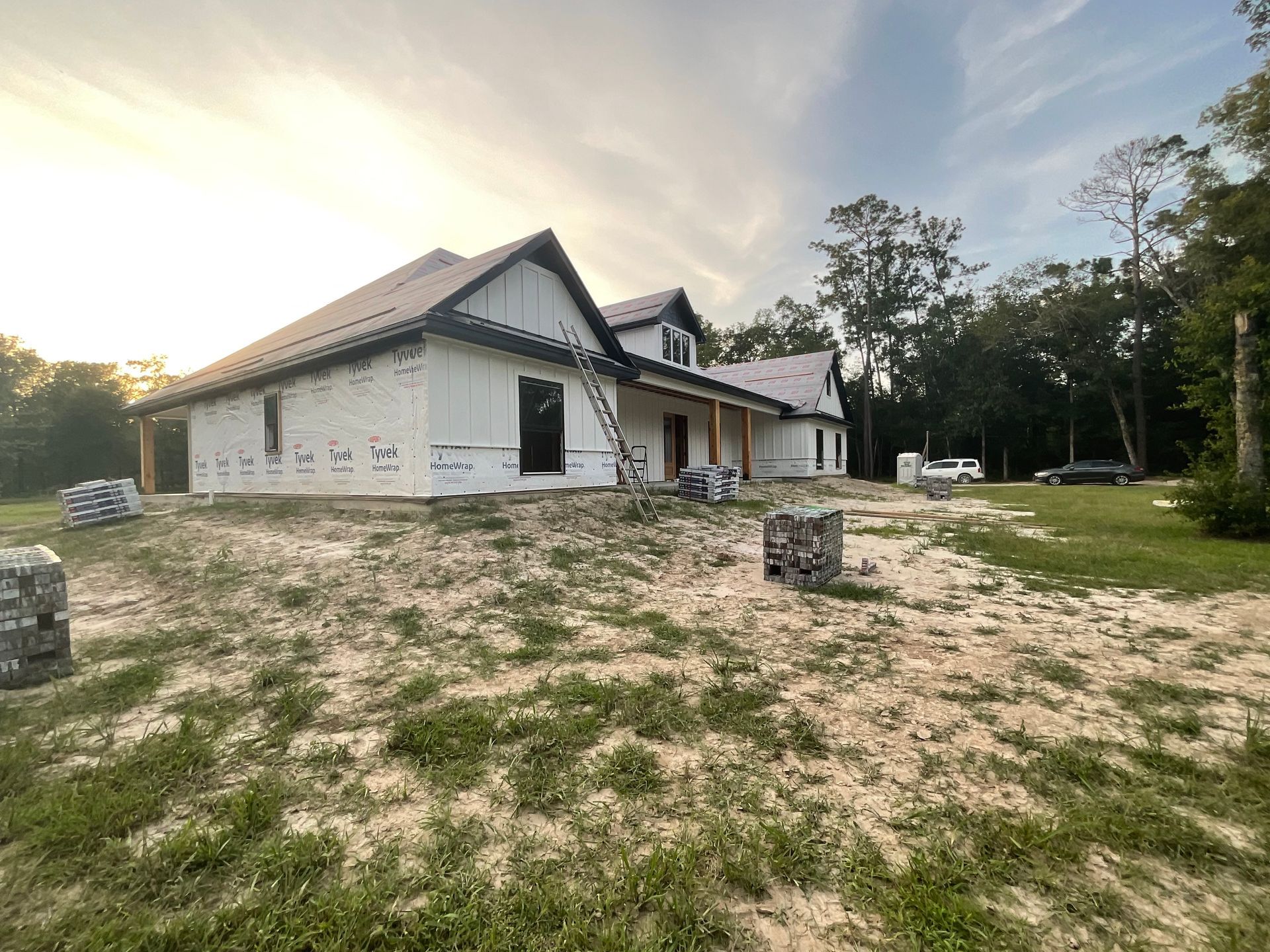 House under construction with white siding, black roof, and tan wooden supports.