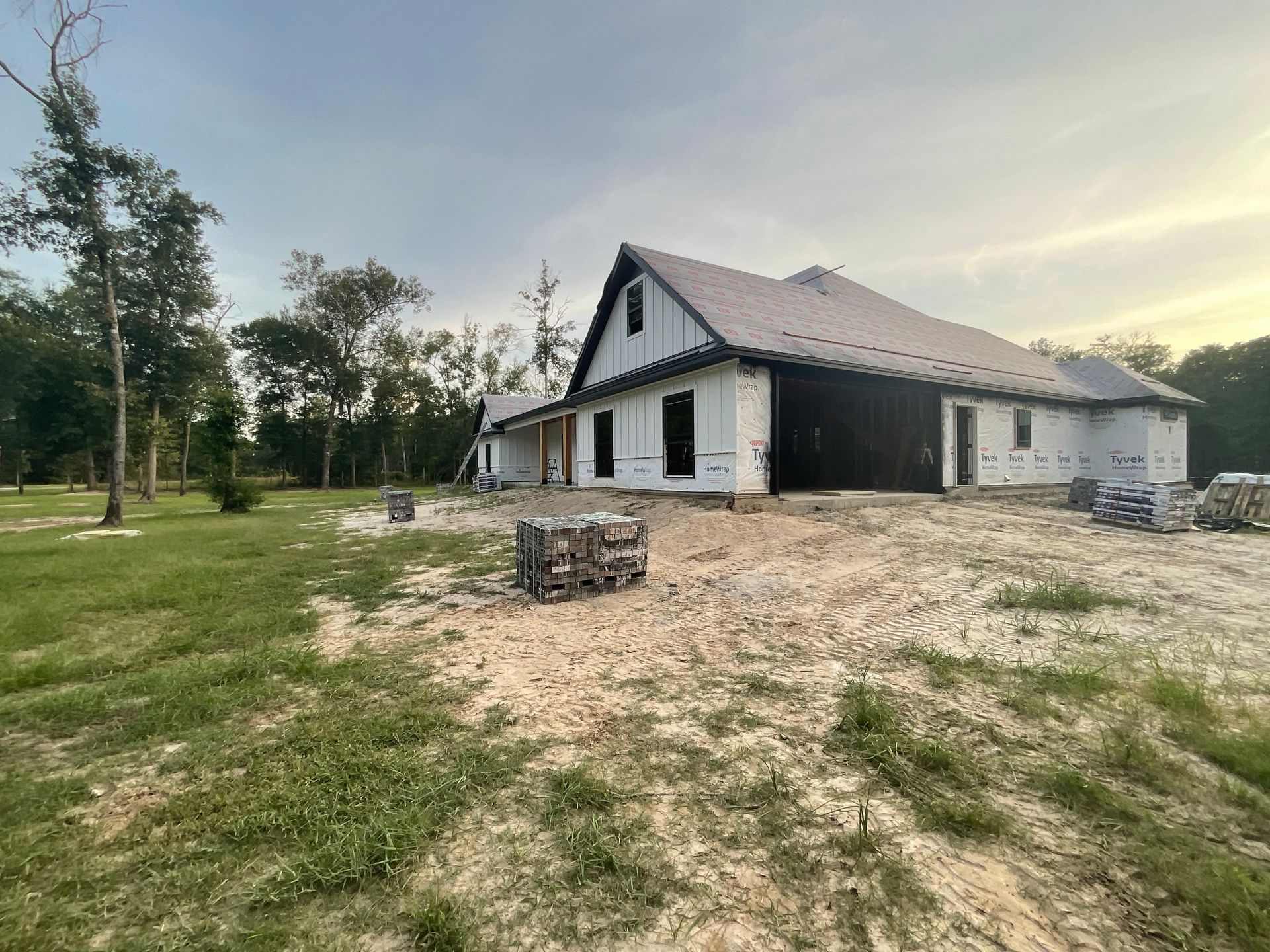 A house under construction with a dark roof and white siding against a cloudy sky.
