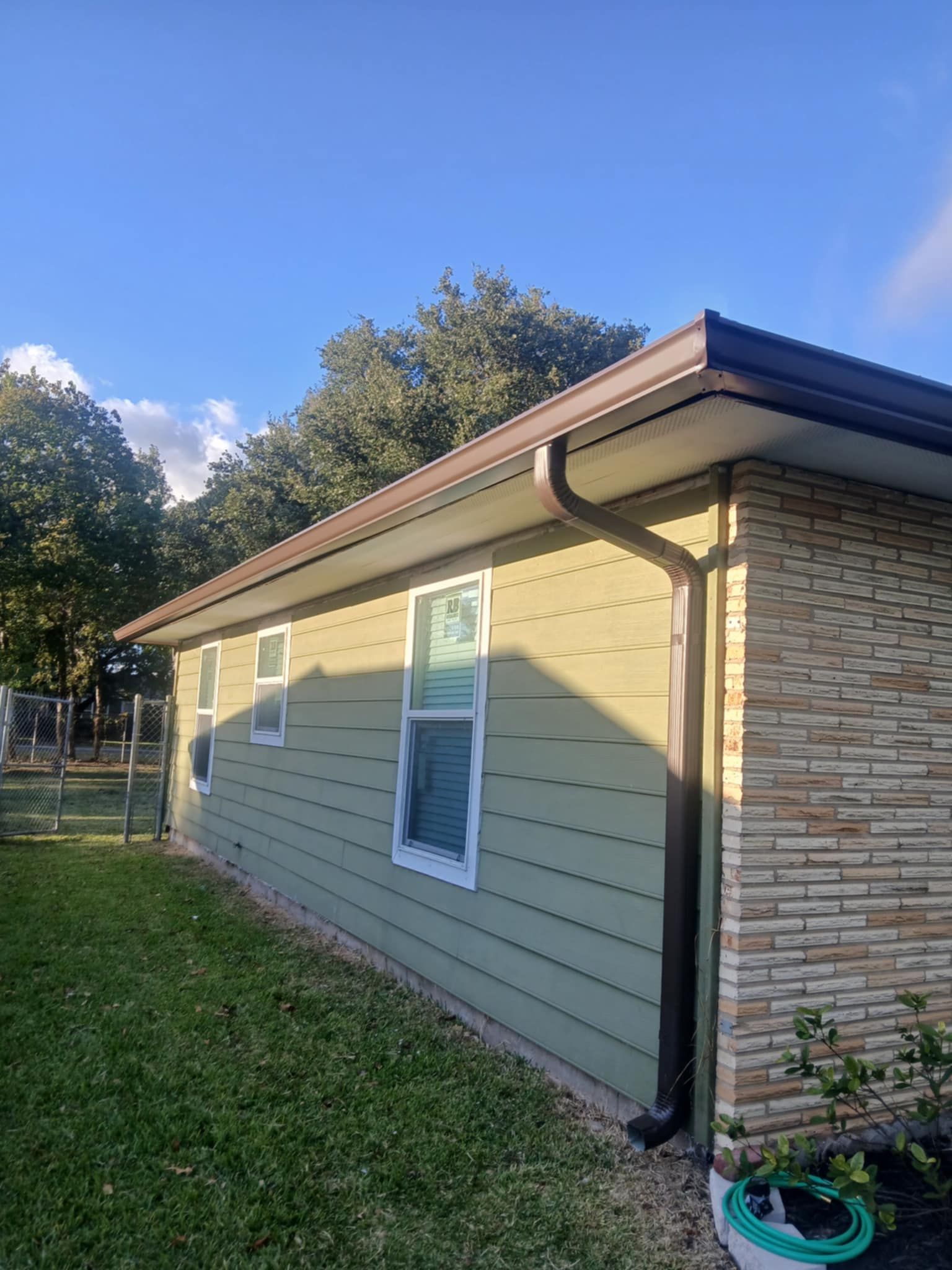 Green-sided house with brown trim and roof, with a brick facade on the right side and a gutter.