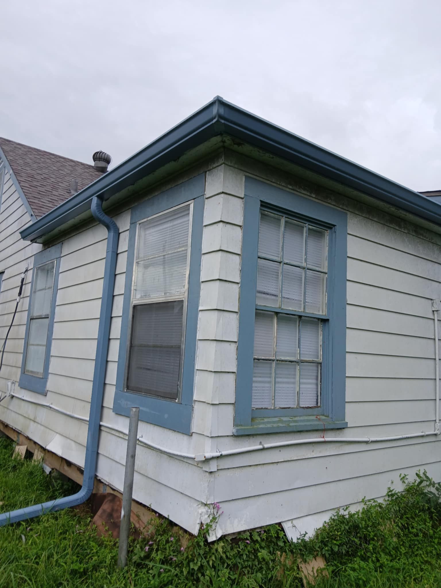 Exterior of a white house with blue trim, windows, and gutters. Cloudy sky overhead.