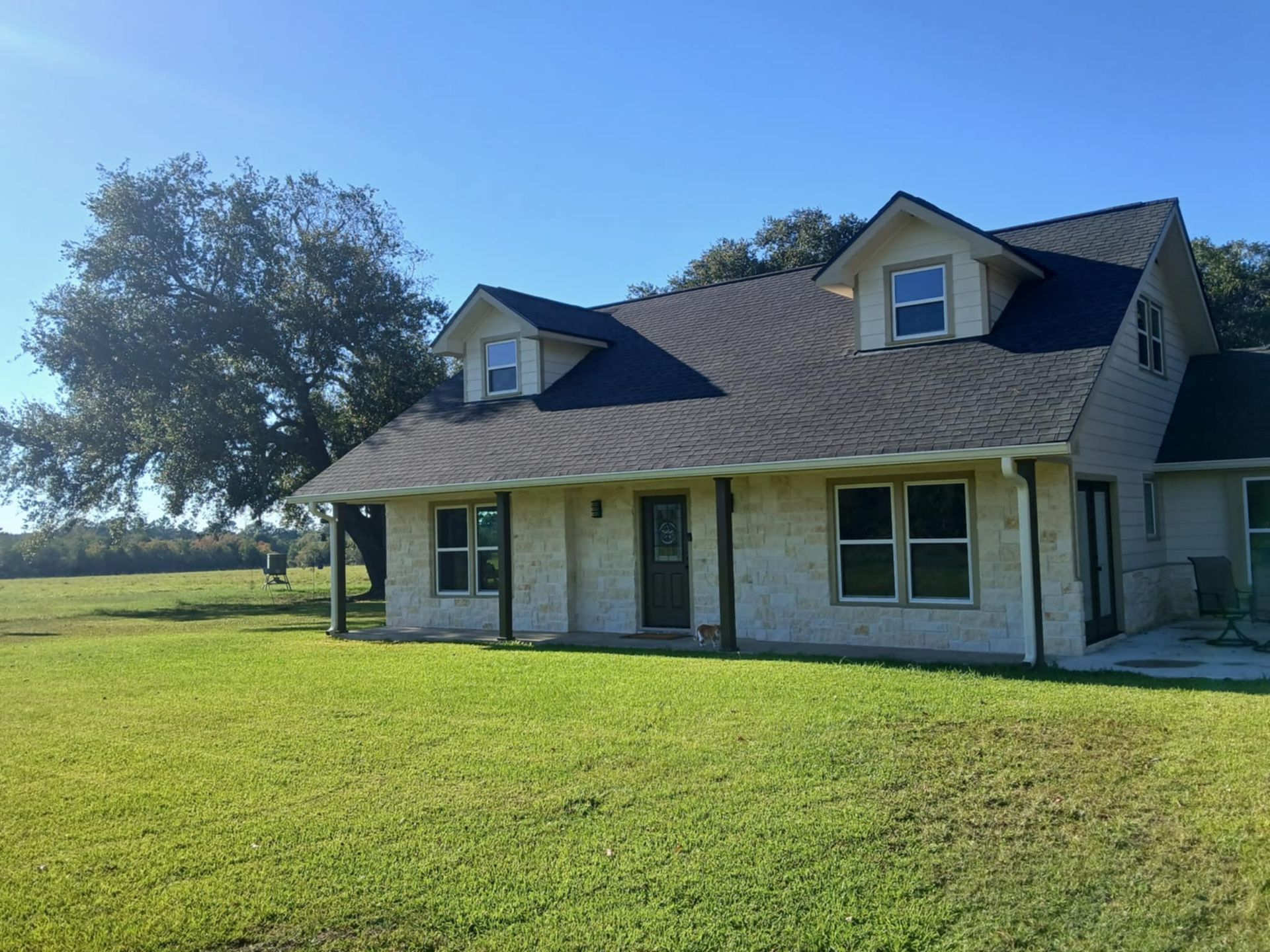 House with dark roof, dormers, light stucco exterior, and green lawn under a blue sky.