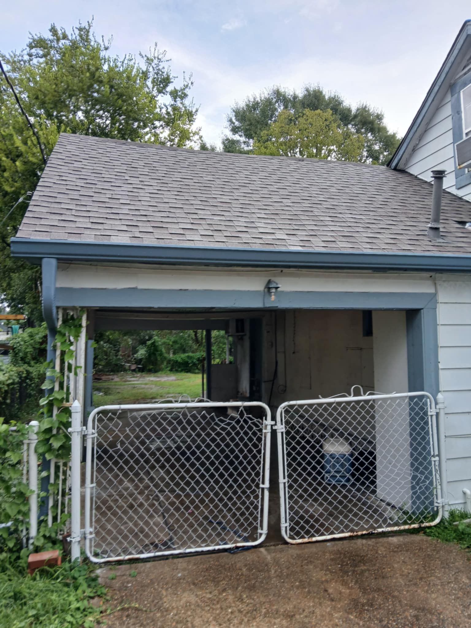 Chain link gate blocks a partially open garage. Roof is gray with blue trim.