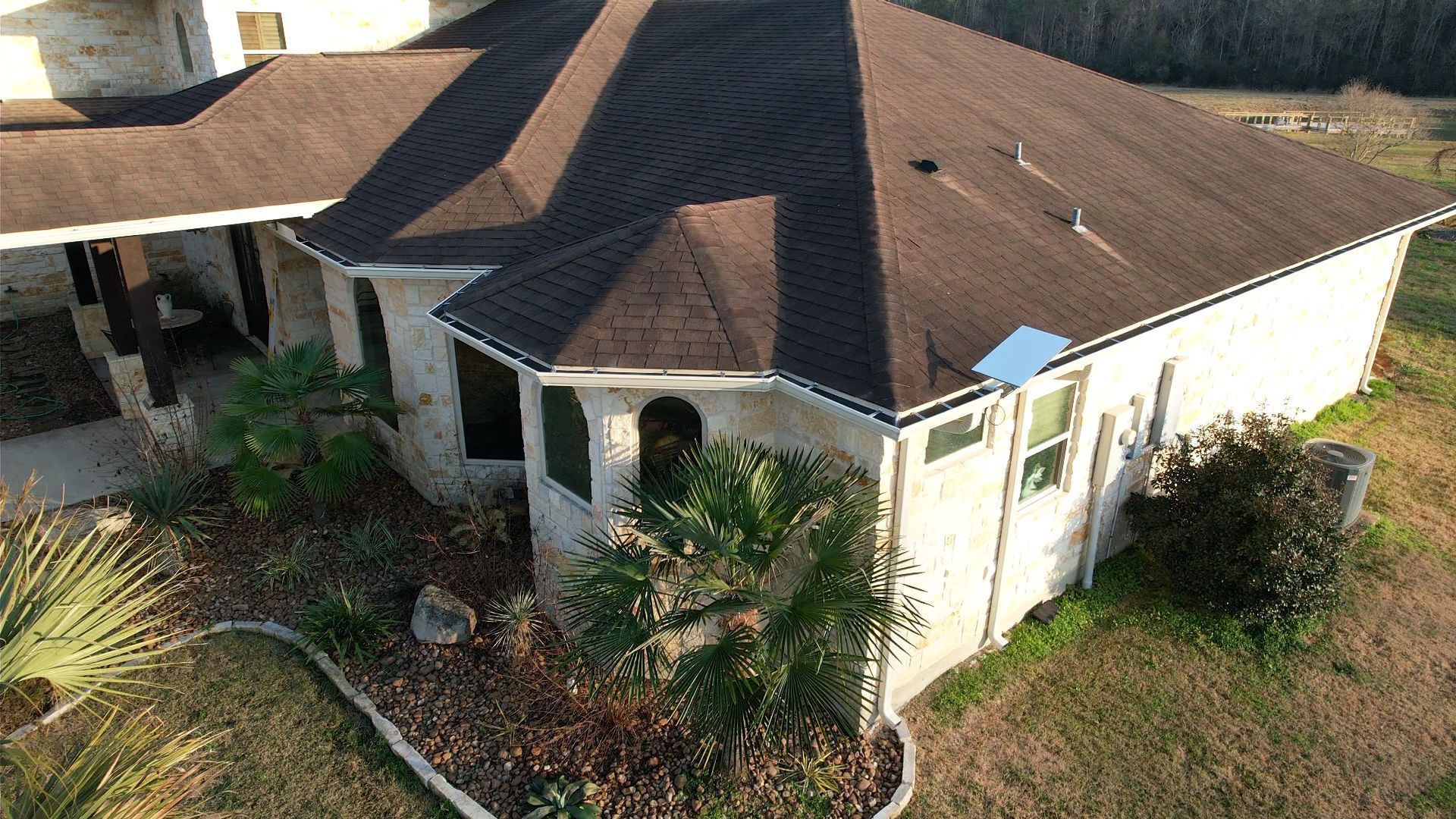 Stone house with a brown roof and surrounding vegetation.