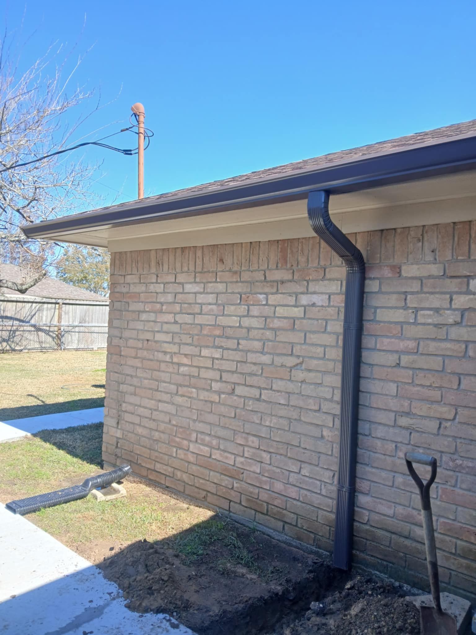 Brown brick building with dark gutters and downspout. Sunny outdoor setting.