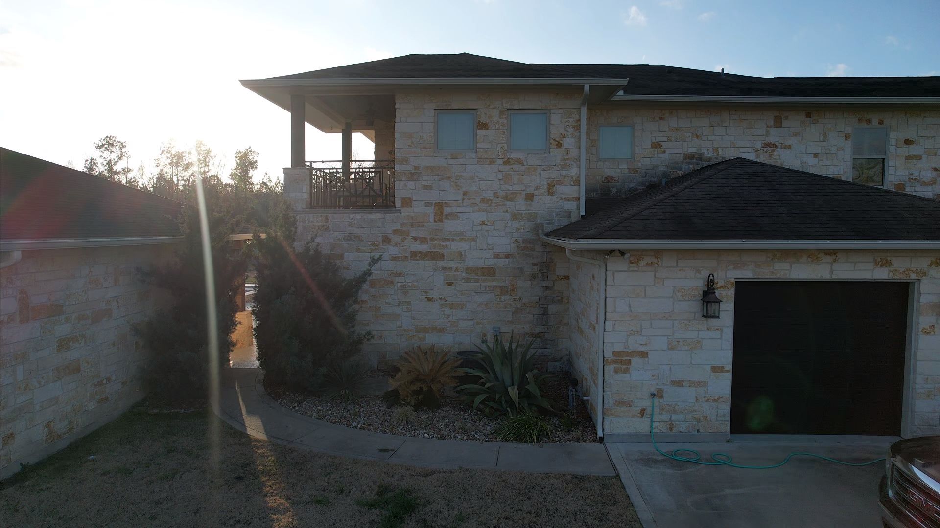 Stone-clad house with a dark garage door, porch, and a view of the sun.