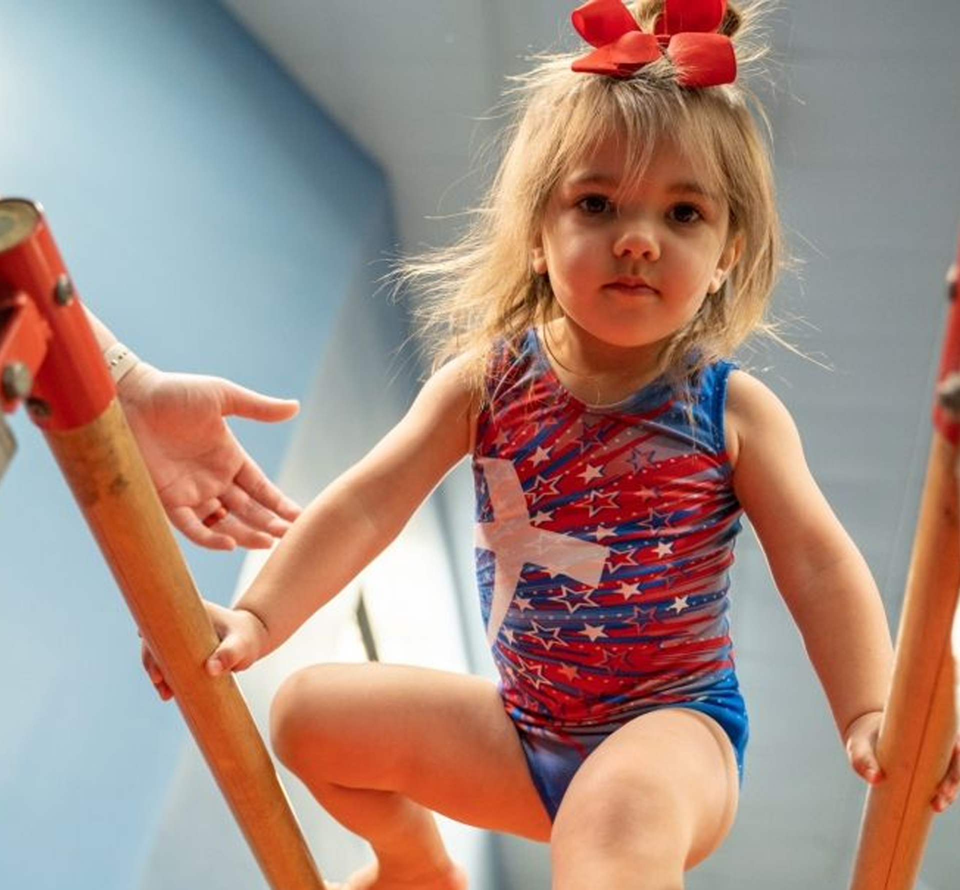 A woman is helping a little girl do a handstand on a red mat.