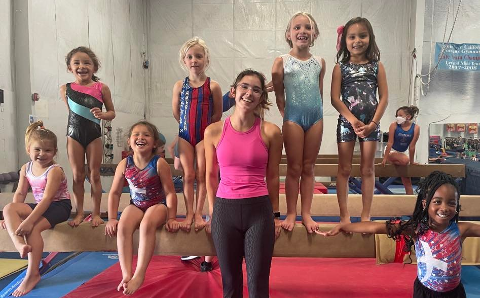 A group of young girls are standing next to each other on a balance beam in a gym.