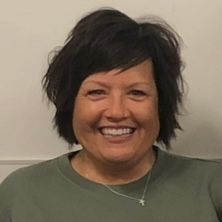 A woman wearing a green shirt and a cross necklace is smiling for the camera.