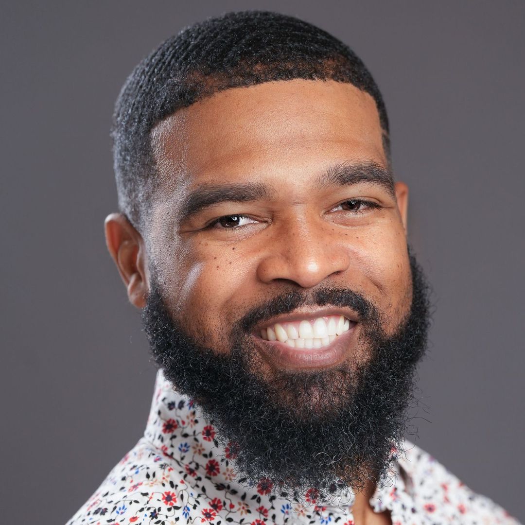 A man with a beard is smiling and wearing a floral shirt.