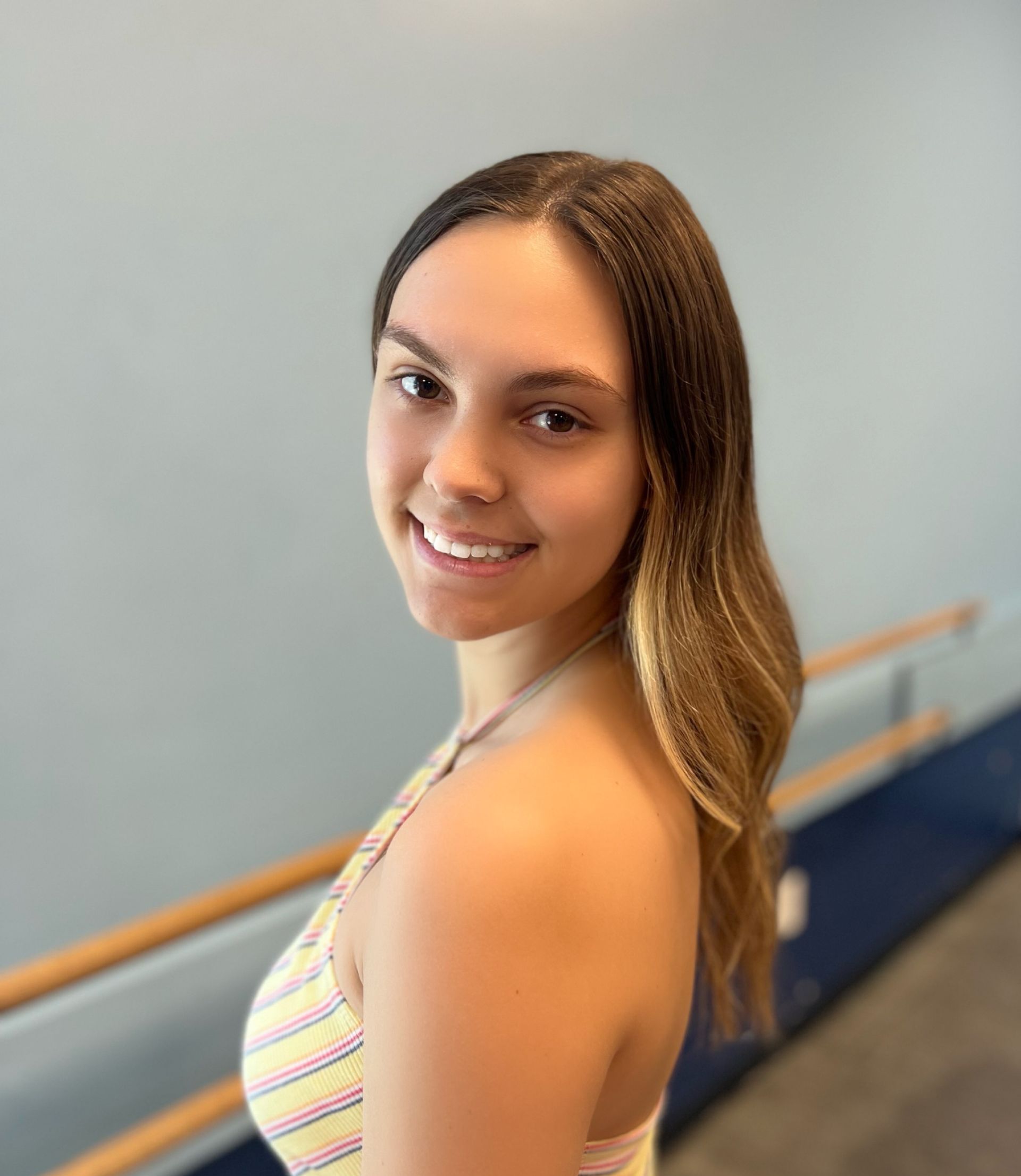 A young woman in a striped top is smiling for the camera in a dance studio.