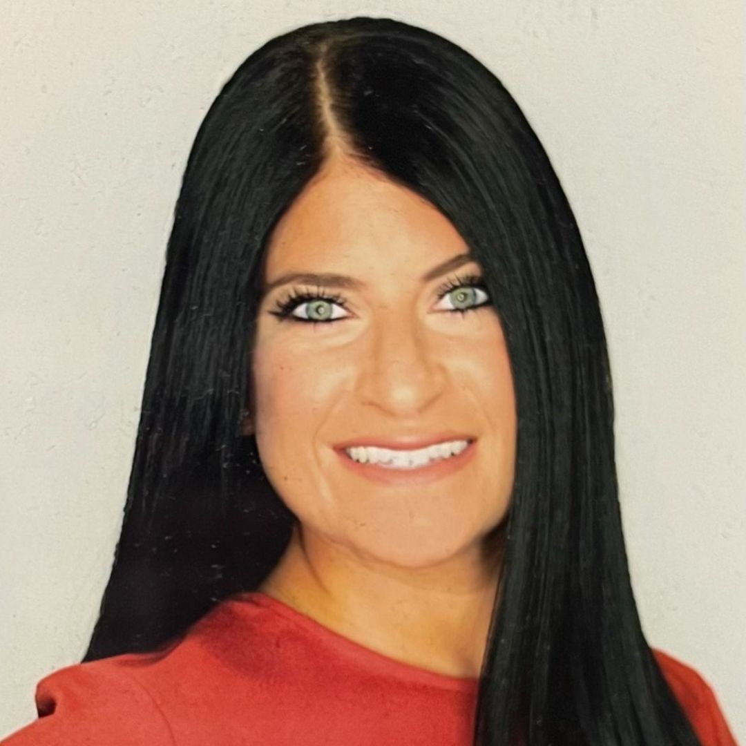 A woman with long black hair is wearing a red shirt and smiling