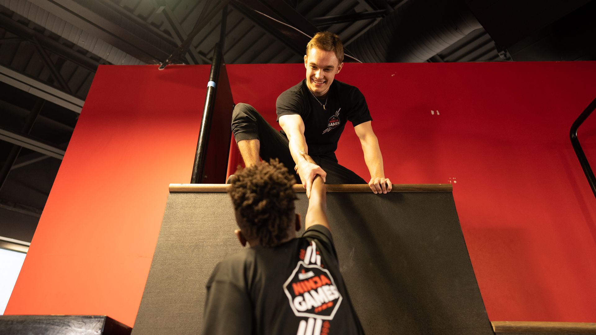 Ninja Coach helping athlete up warp wall.