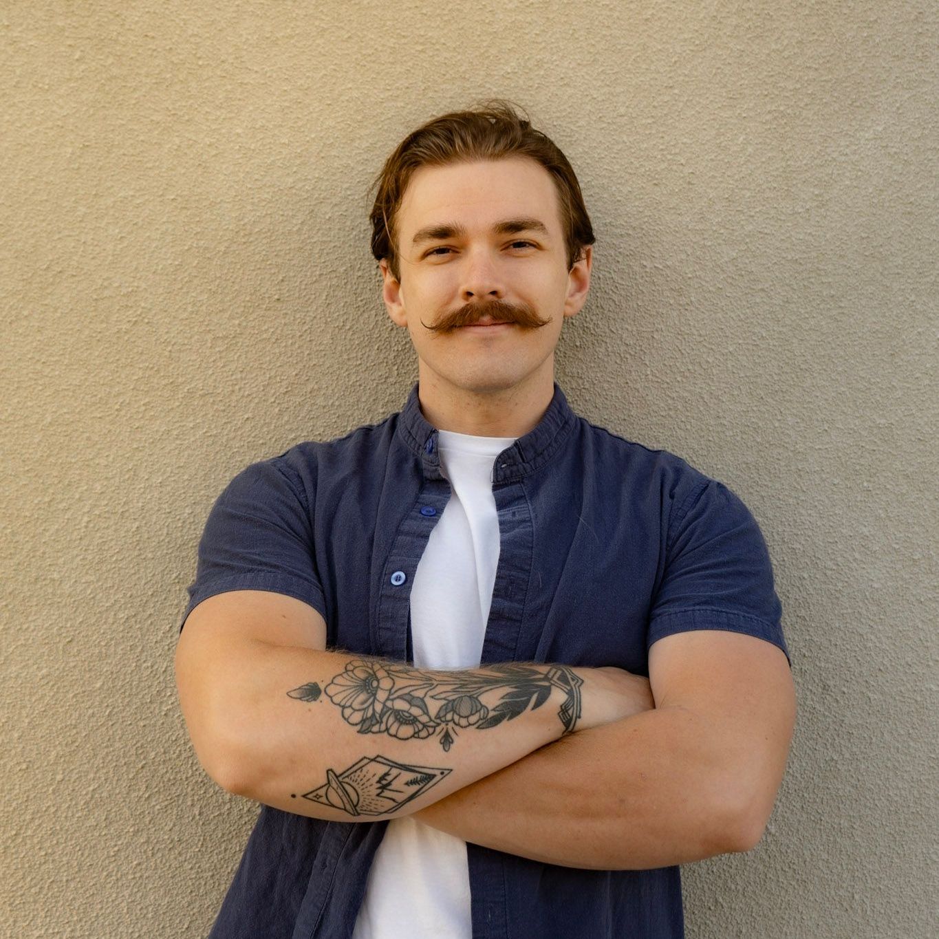 A man with a mustache is standing with his arms crossed