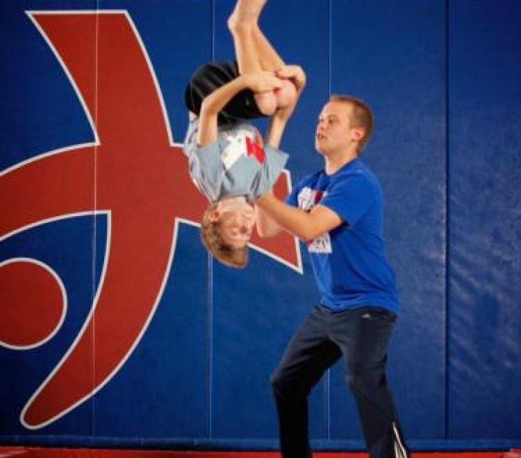 A man is helping a young boy do a handstand in front of a large letter h