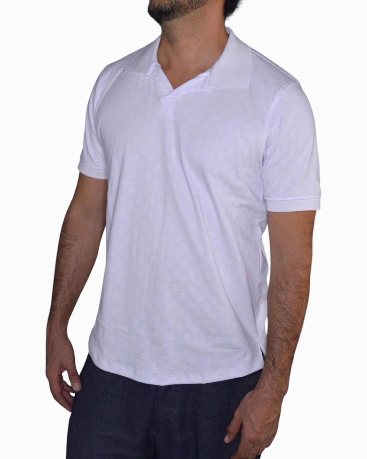 Hombre vestido con un polo blanco, de pie sobre un fondo blanco.