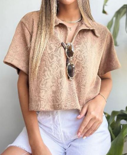 Una mujer que viste una camisa marrón y pantalones cortos blancos está sentada junto a una planta.