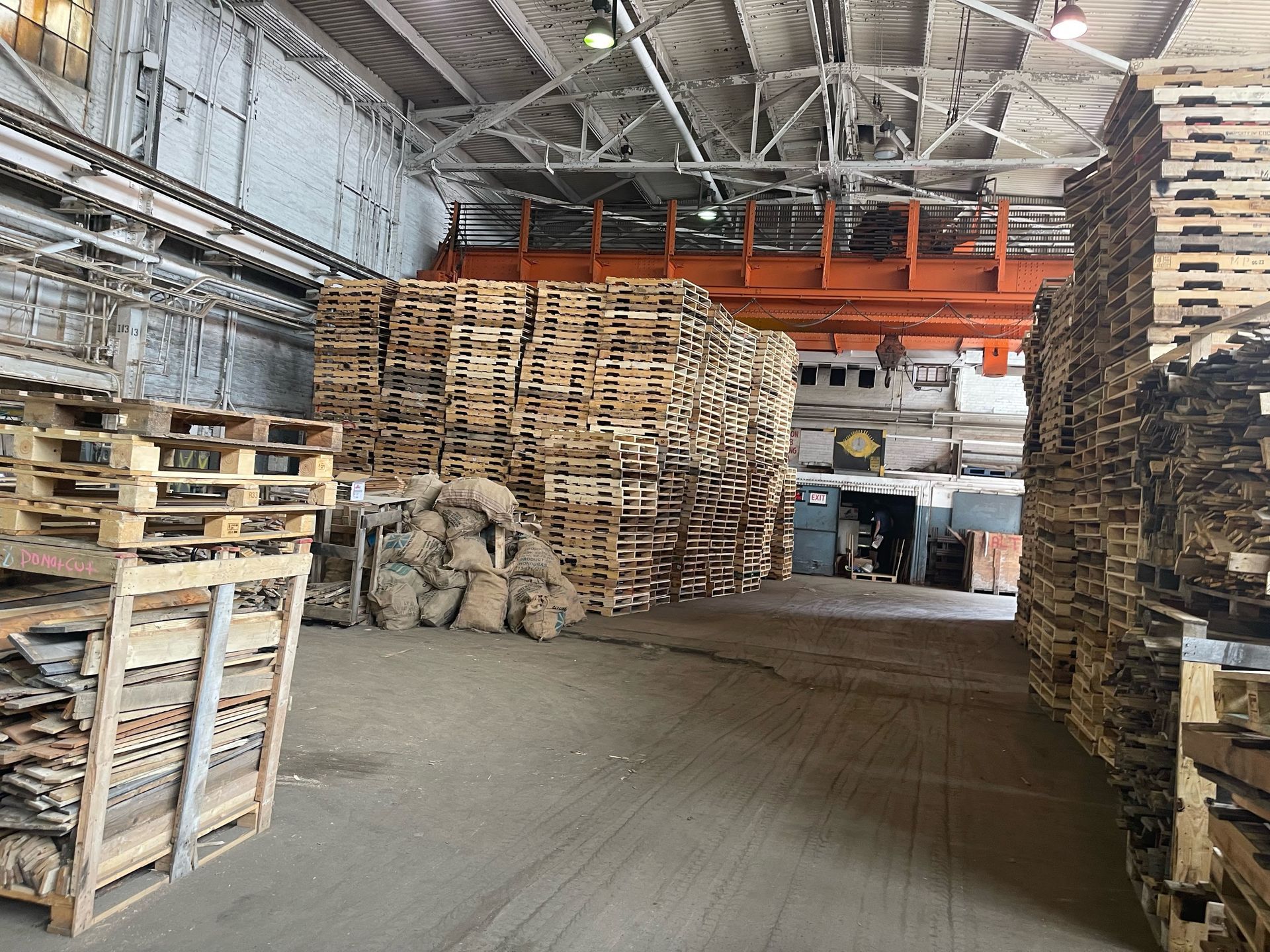 Warehouse interior with stacks of wooden pallets. A crane is visible in the background.