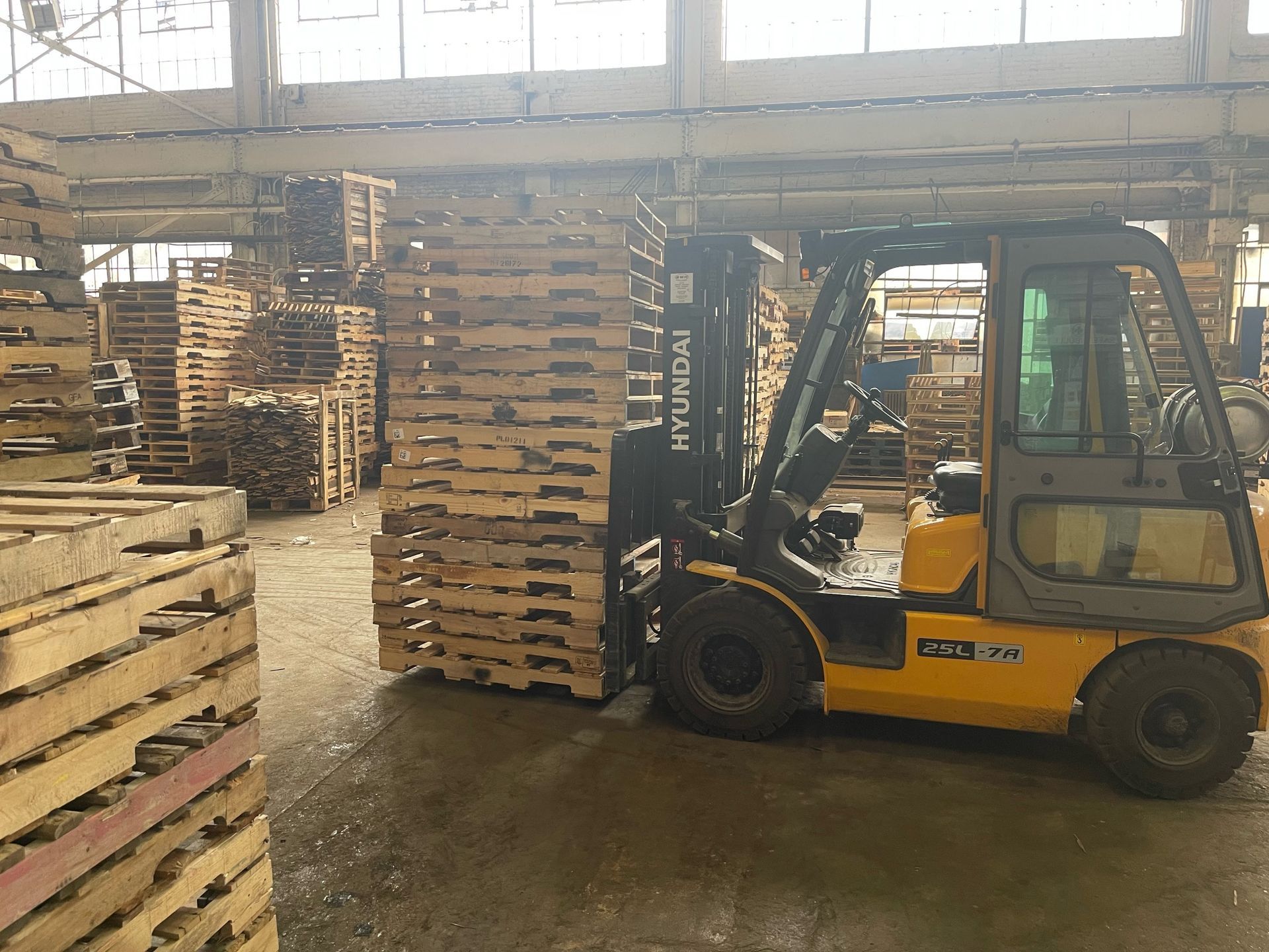 Yellow forklift carrying a stack of wooden pallets inside a warehouse.