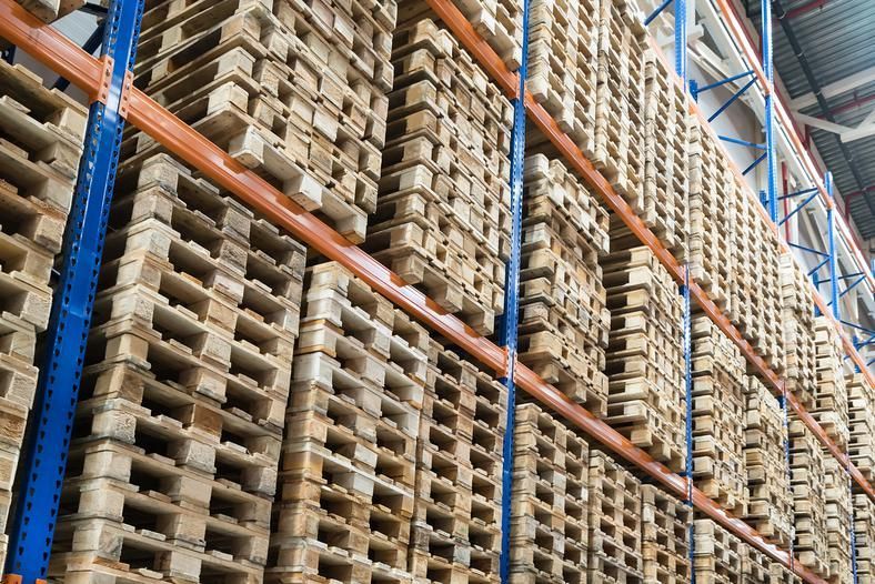 Wooden pallets stacked high in a warehouse storage rack, steel beams, neutral lighting.