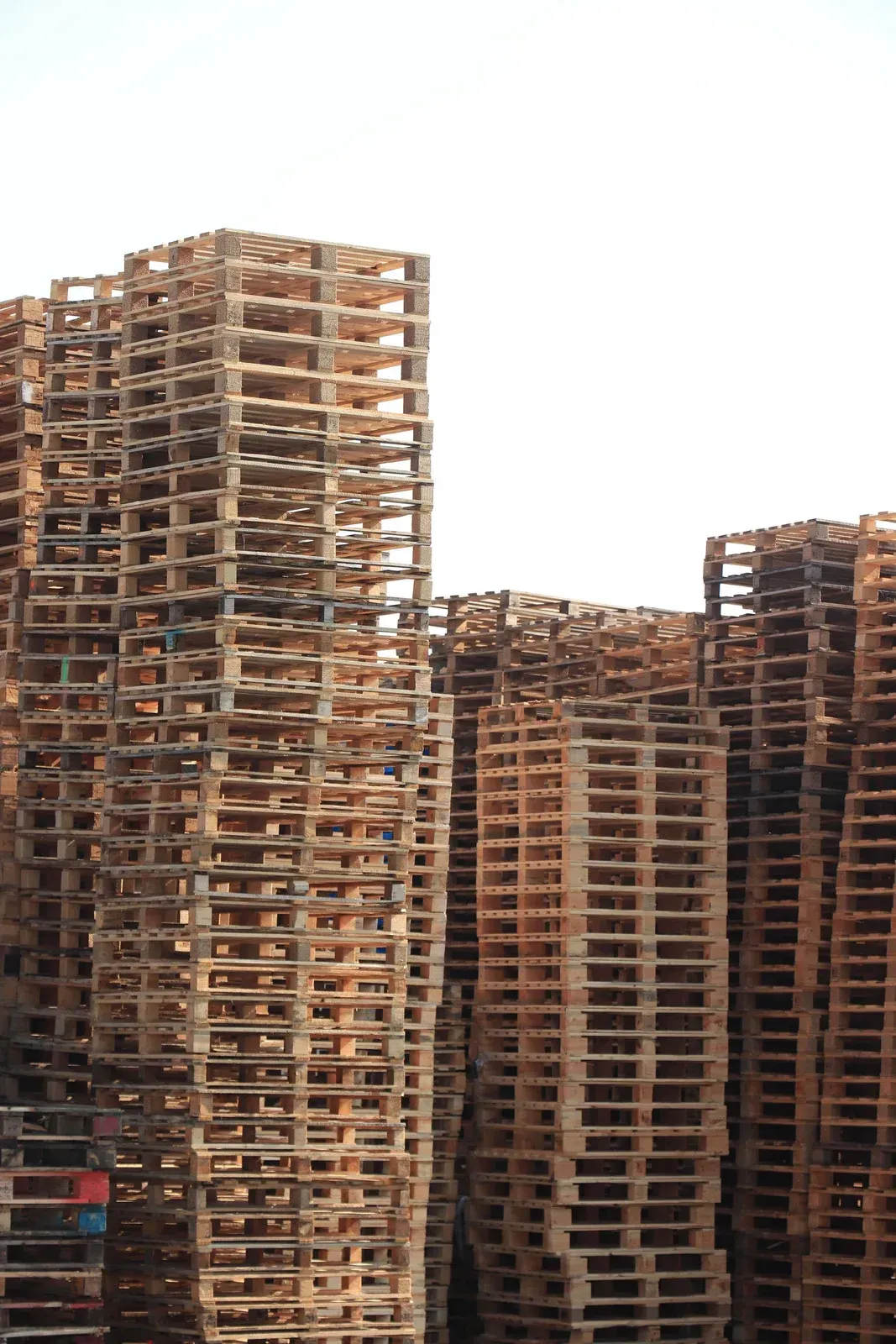 Stacks of weathered wooden shipping pallets against a bright sky.