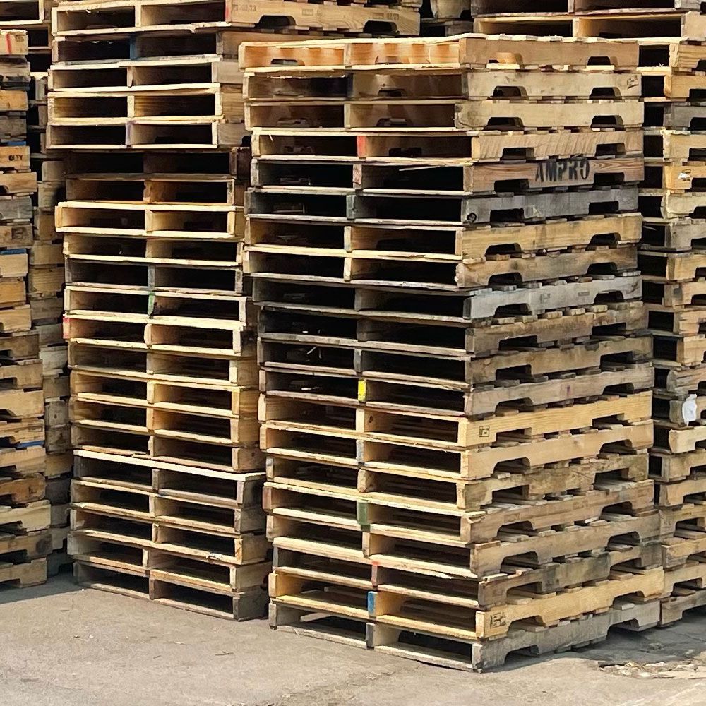 Stacks of wooden shipping pallets in an outdoor setting, possibly a warehouse.
