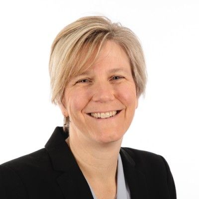 Woman with short blonde hair, smiling, wearing a black blazer.