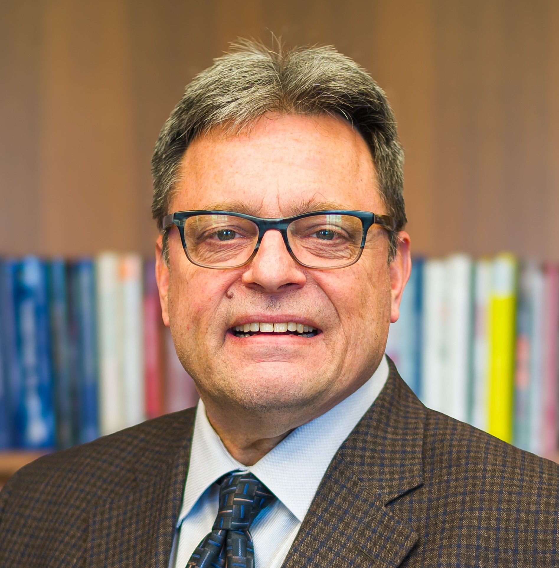 Man in glasses and suit smiling in front of a bookshelf.